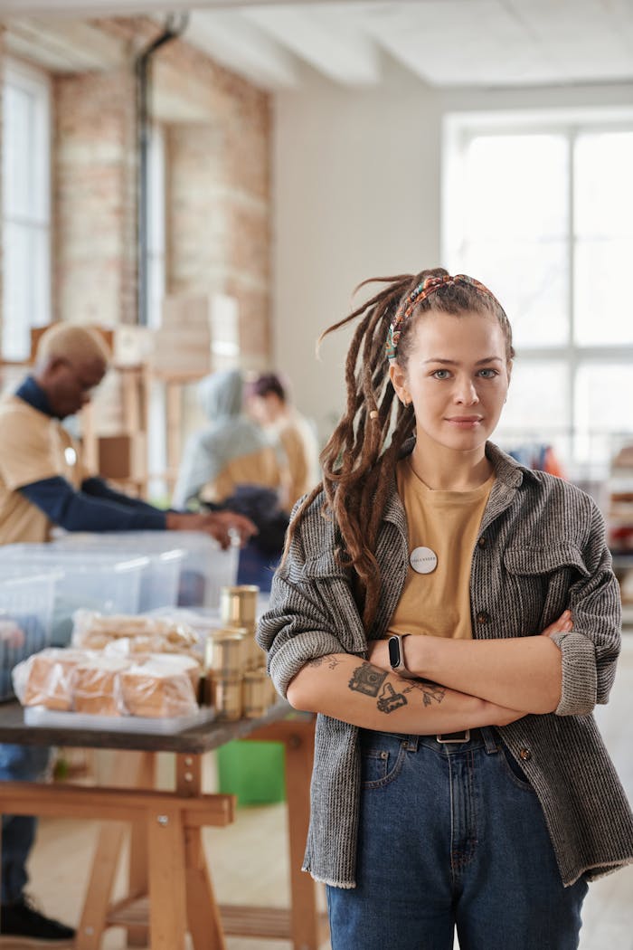 Young woman with dreadlocks volunteering in a thrift store, arms crossed, smiling confidently.